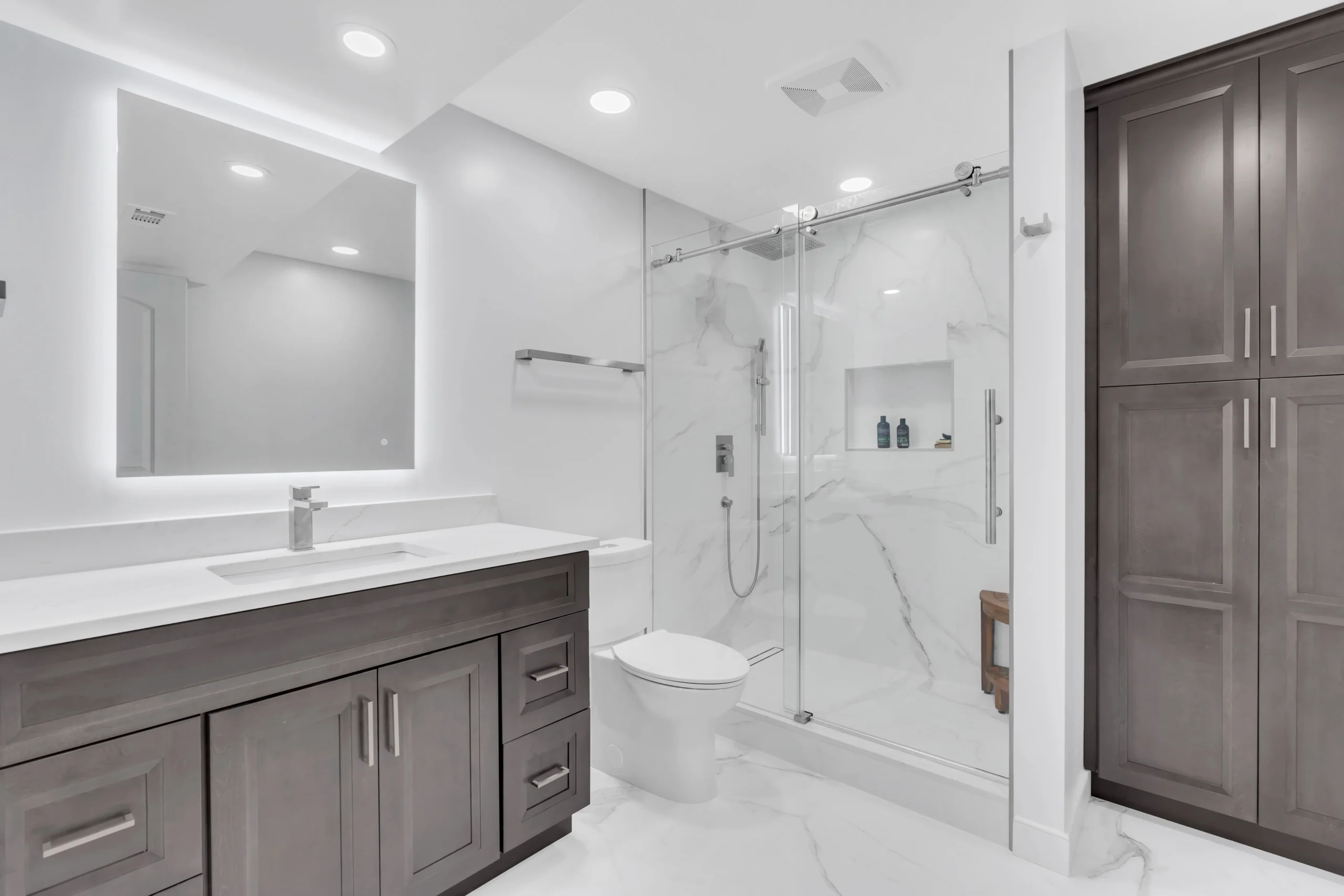Modern bathroom with dark wood vanity, large mirror, and glass-enclosed shower with marble walls and floors